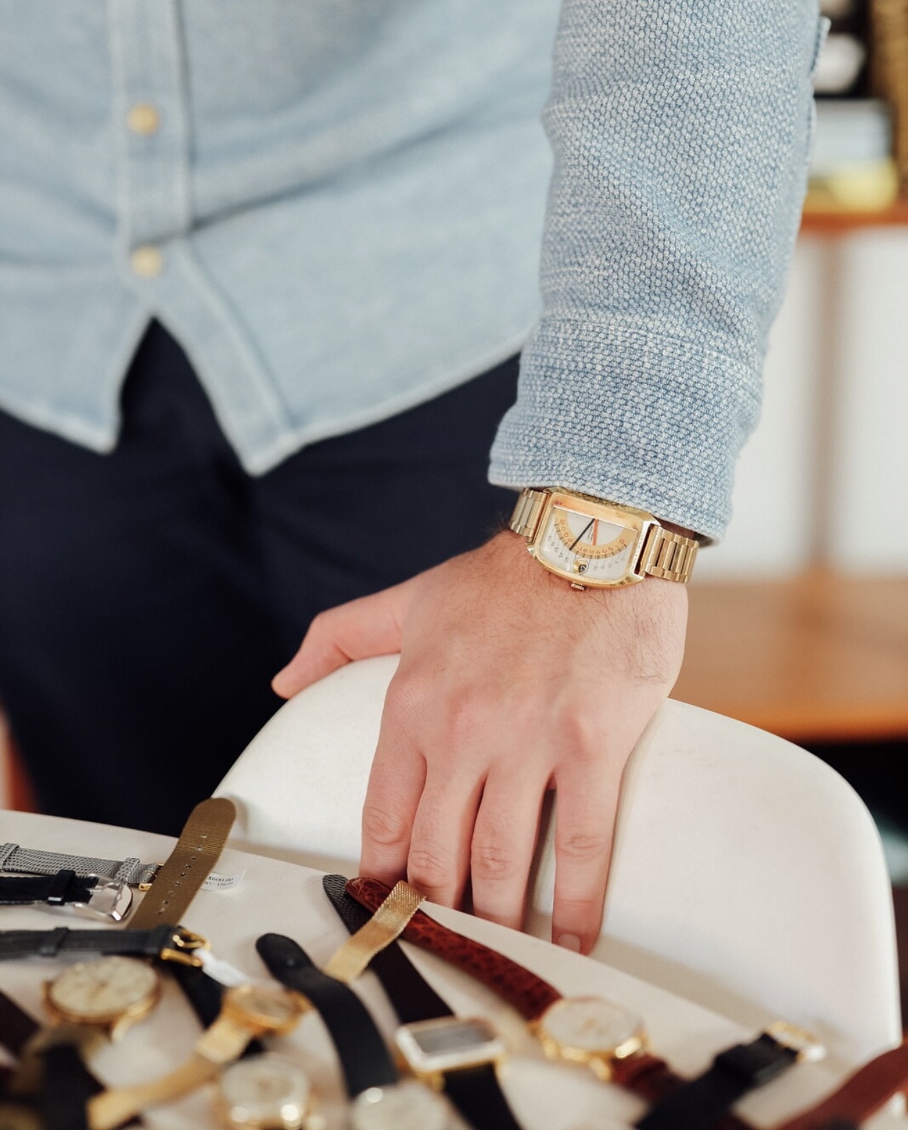 Gold rectangular vintage watch worn with denim shirt over a tray of straps